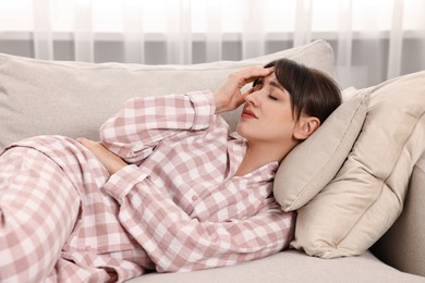 Photo of Upset woman suffering from headache on sofa at home