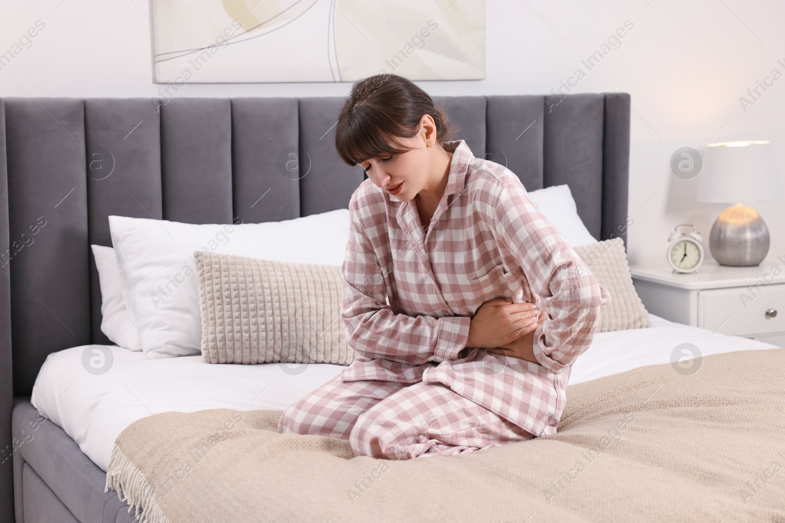 Photo of Upset woman suffering from abdominal pain on bed at home