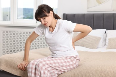 Photo of Upset woman suffering from back pain on bed at home