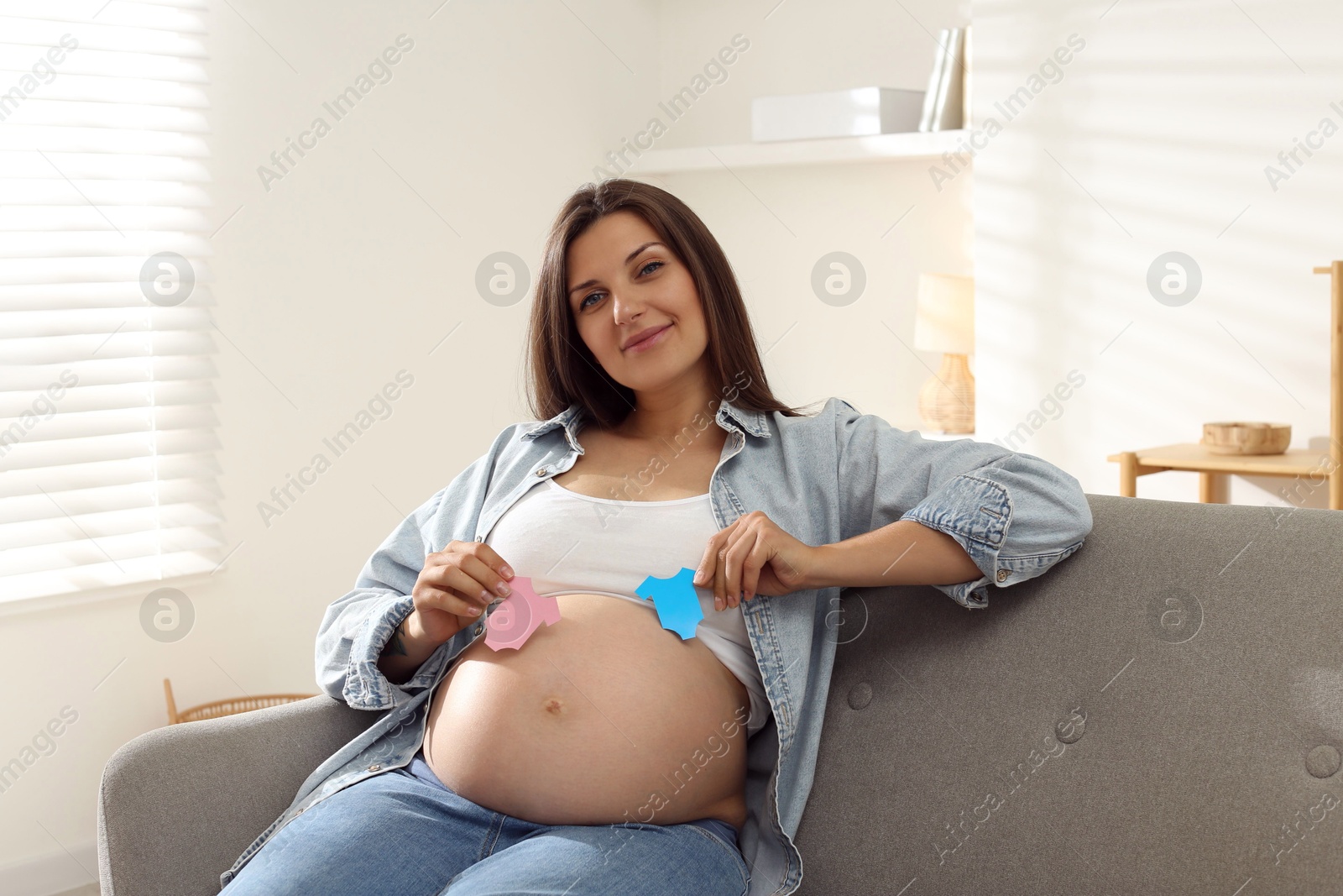 Photo of Beautiful pregnant woman with paper hearts on sofa at home. Expecting twins