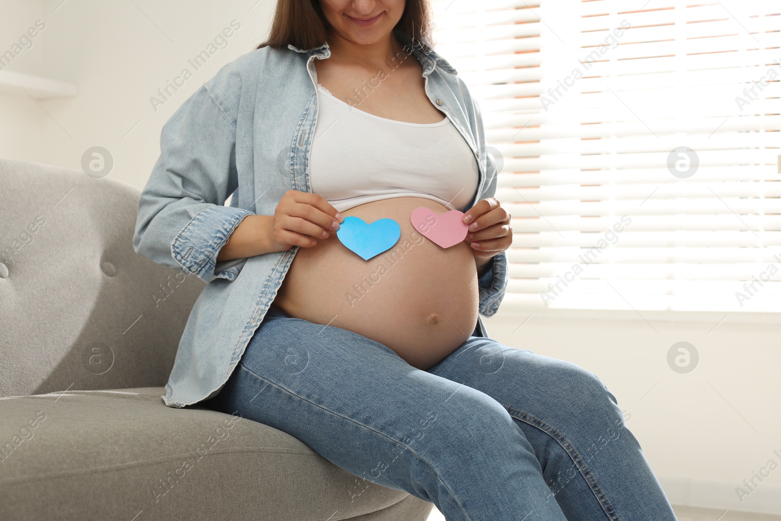 Photo of Pregnant woman with paper hearts on sofa at home, closeup. Expecting twins