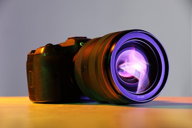 Photo of Modern photo camera in neon lights on table