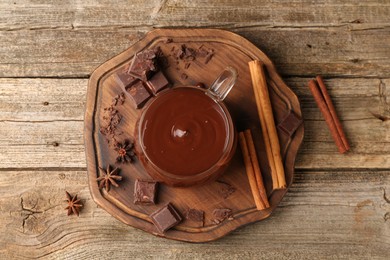 Tasty melted chocolate in cup and spices on wooden table, flat lay