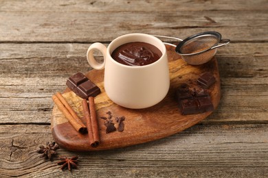 Photo of Tasty melted chocolate in cup and spices on wooden table, closeup