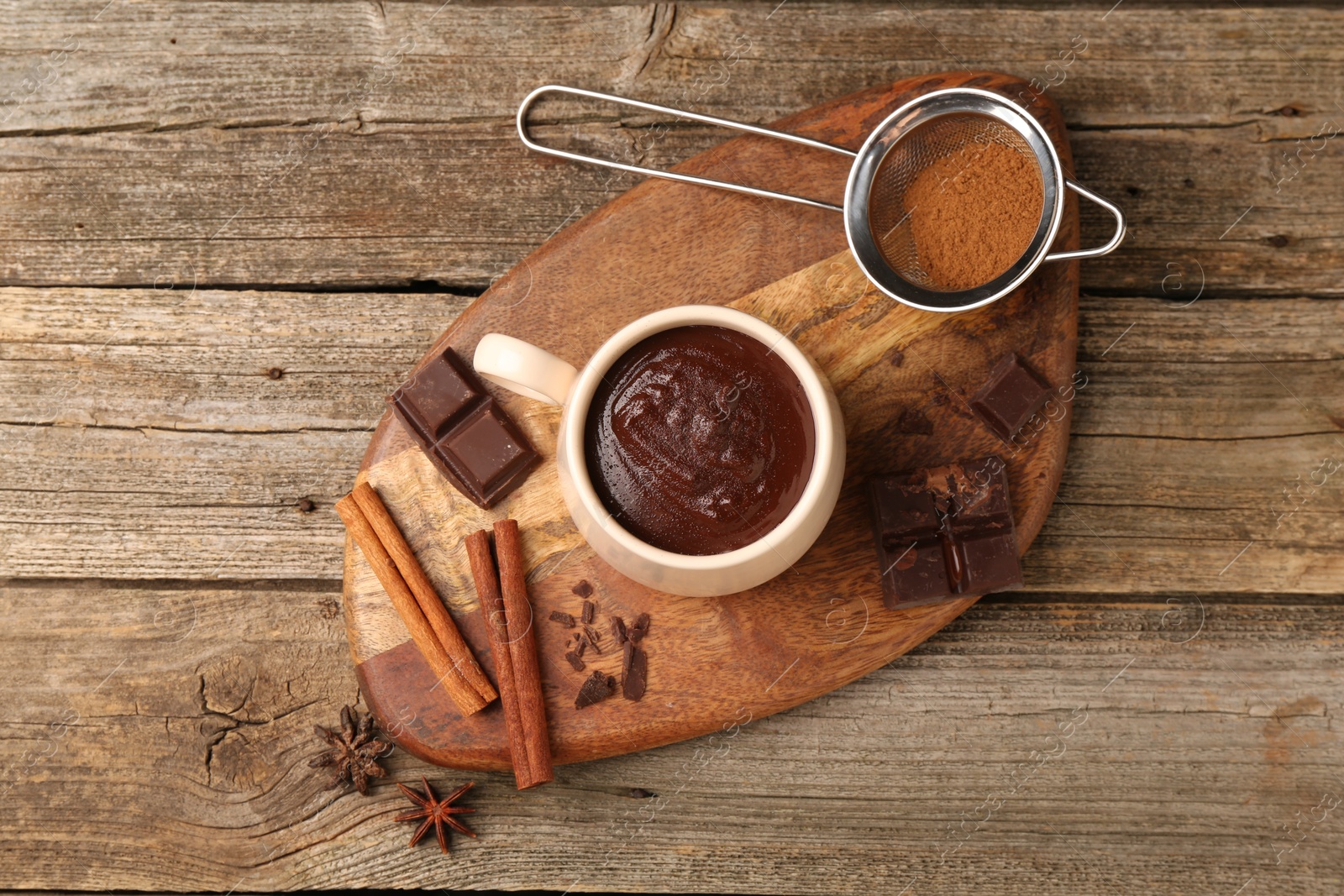 Photo of Tasty melted chocolate in cup and spices on wooden table, top view