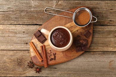 Photo of Tasty melted chocolate in cup and spices on wooden table, top view