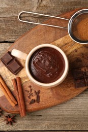 Photo of Tasty melted chocolate in cup and spices on wooden table, top view