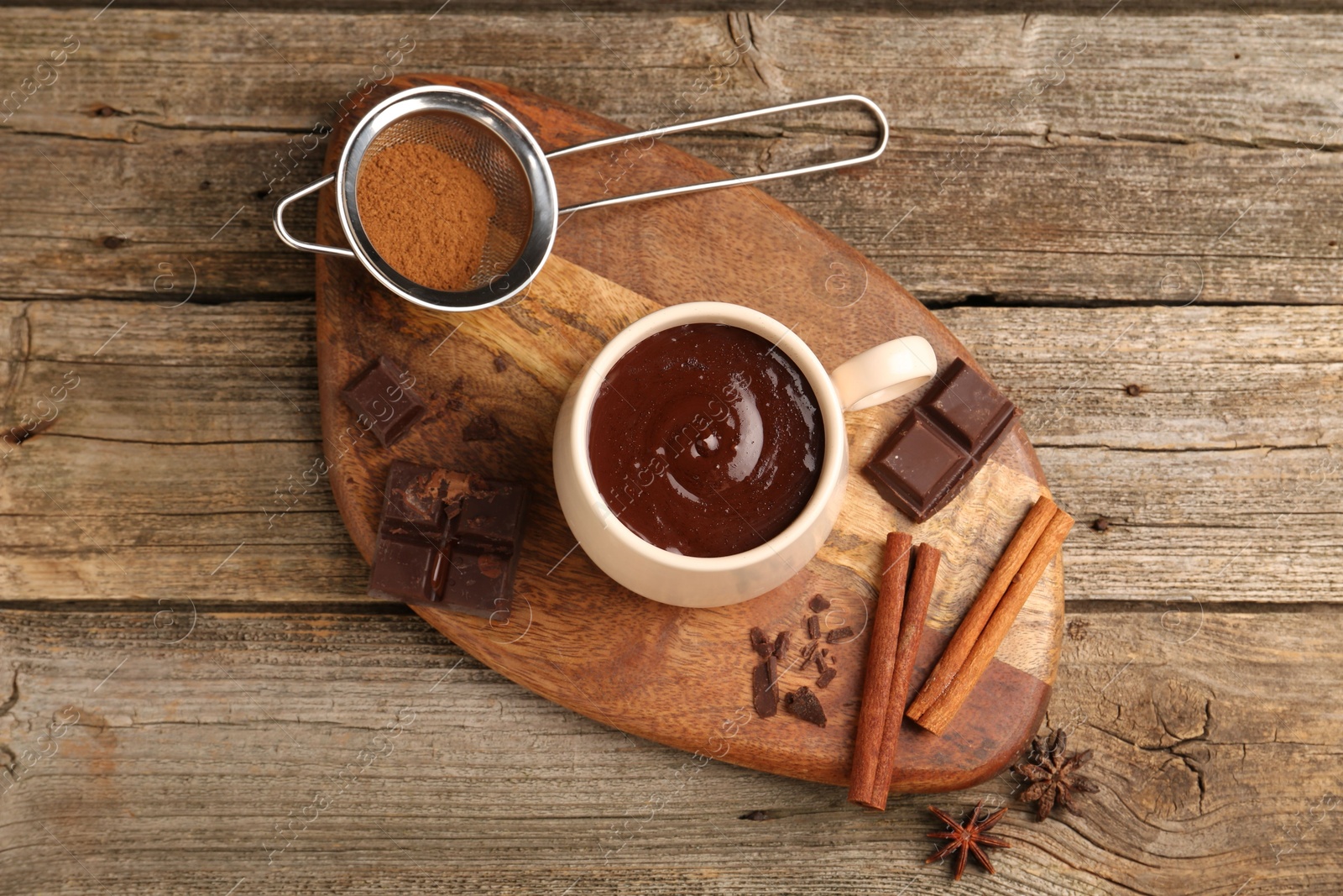 Photo of Tasty melted chocolate in cup and spices on wooden table, flat lay