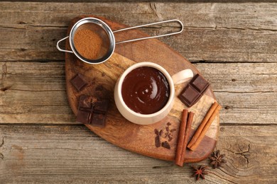 Tasty melted chocolate in cup and spices on wooden table, flat lay