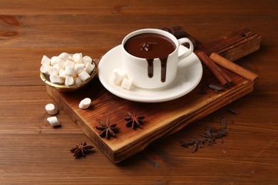 Photo of Tasty melted chocolate in cup, marshmallows and spices on wooden table