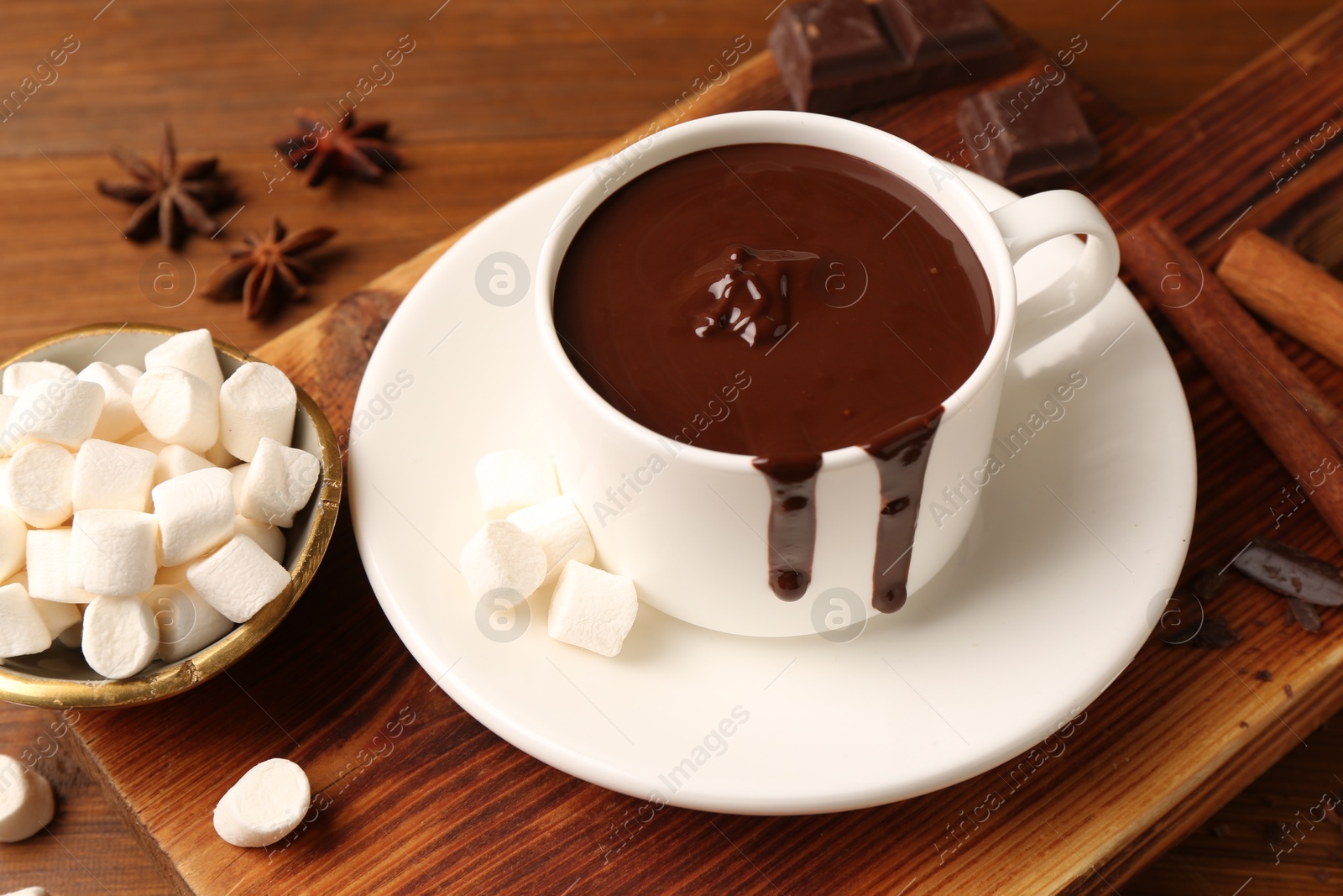 Photo of Tasty melted chocolate in cup and marshmallows on wooden table, closeup