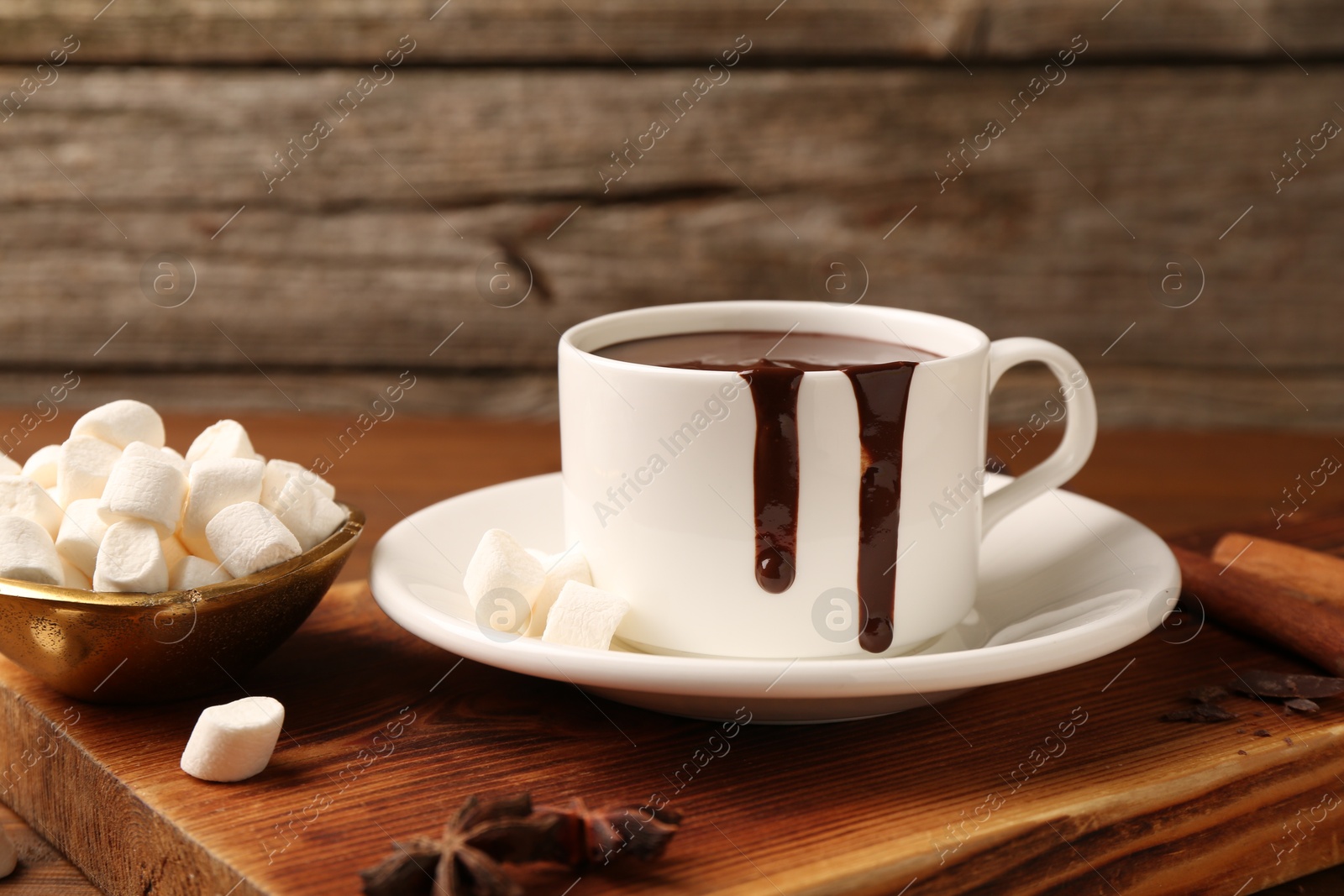 Photo of Tasty melted chocolate in cup and marshmallows on wooden table, closeup