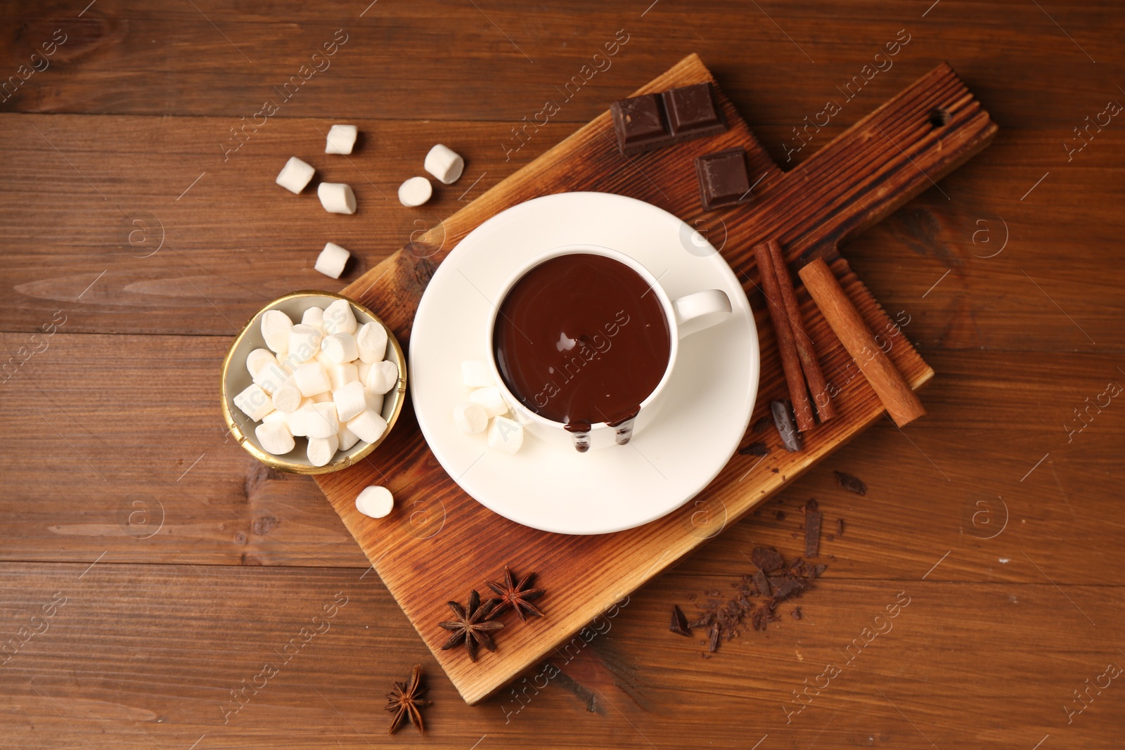 Photo of Tasty melted chocolate in cup, marshmallows and spices on wooden table, flat lay