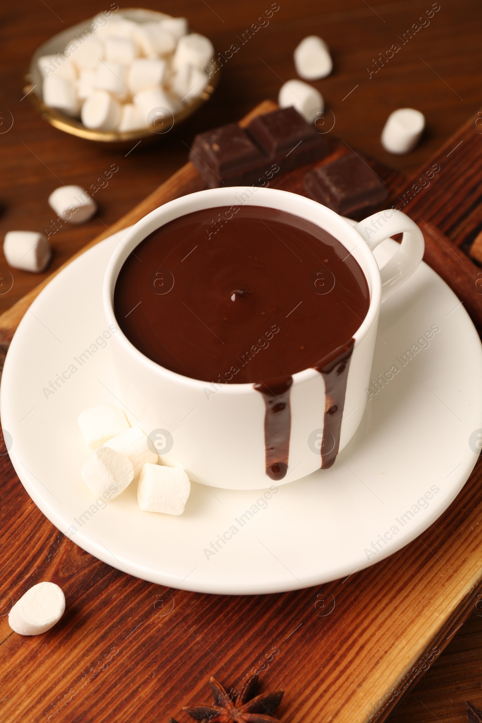 Photo of Tasty melted chocolate in cup and marshmallows on wooden table