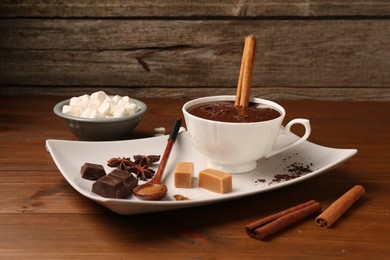 Photo of Tasty melted chocolate in cup, marshmallows, candies and spices on wooden table