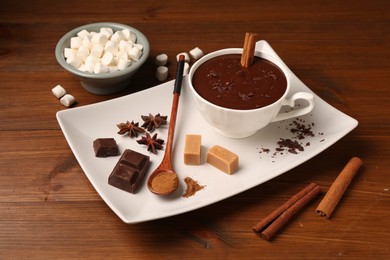 Photo of Tasty melted chocolate in cup, marshmallows, candies and spices on wooden table