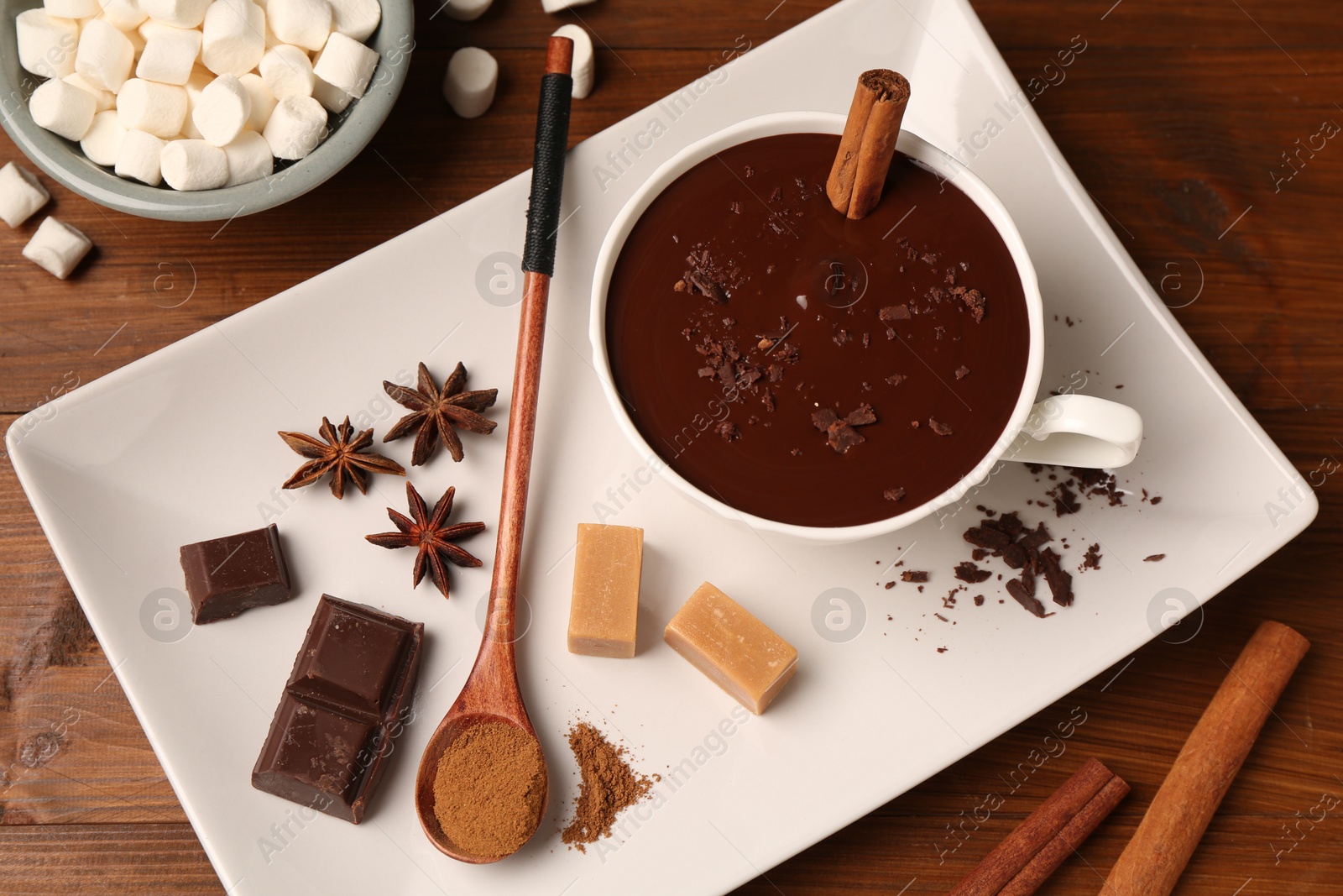 Photo of Tasty melted chocolate in cup, marshmallows, candies and spices on wooden table, flat lay