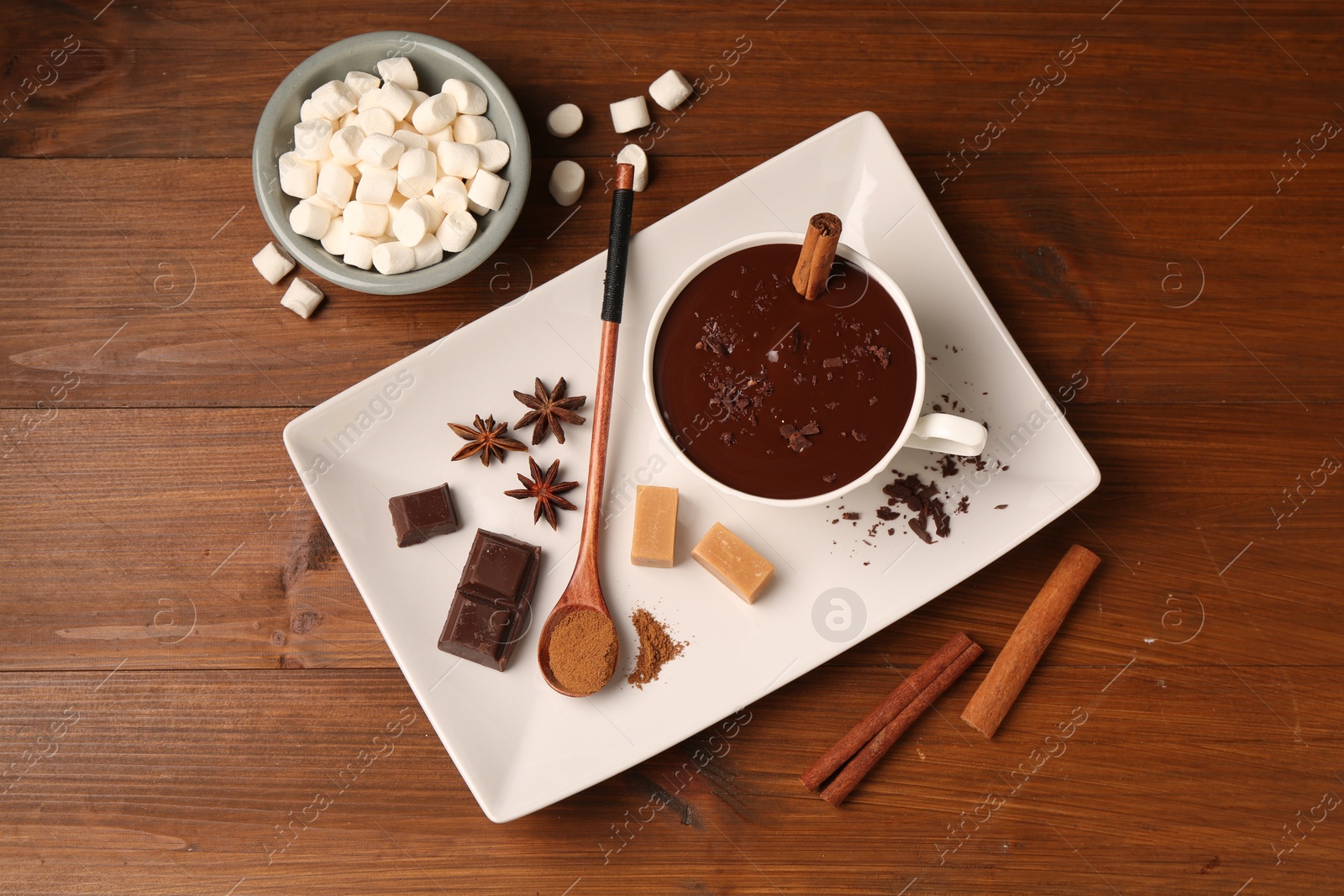 Photo of Tasty melted chocolate in cup, marshmallows, candies and spices on wooden table, flat lay