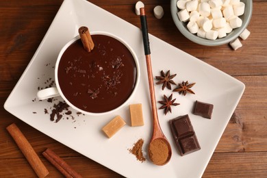 Photo of Tasty melted chocolate in cup, marshmallows, candies and spices on wooden table, flat lay