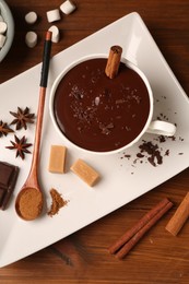 Photo of Tasty melted chocolate in cup, marshmallows, candies and spices on wooden table, flat lay