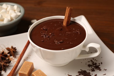 Photo of Tasty melted chocolate with cinnamon stick in cup on table, closeup