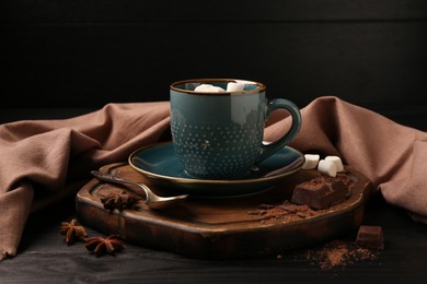 Photo of Tasty melted chocolate with marshmallows in cup and spices on dark wooden table, closeup