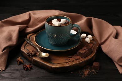 Photo of Tasty melted chocolate with marshmallows in cup and spices on dark wooden table, closeup