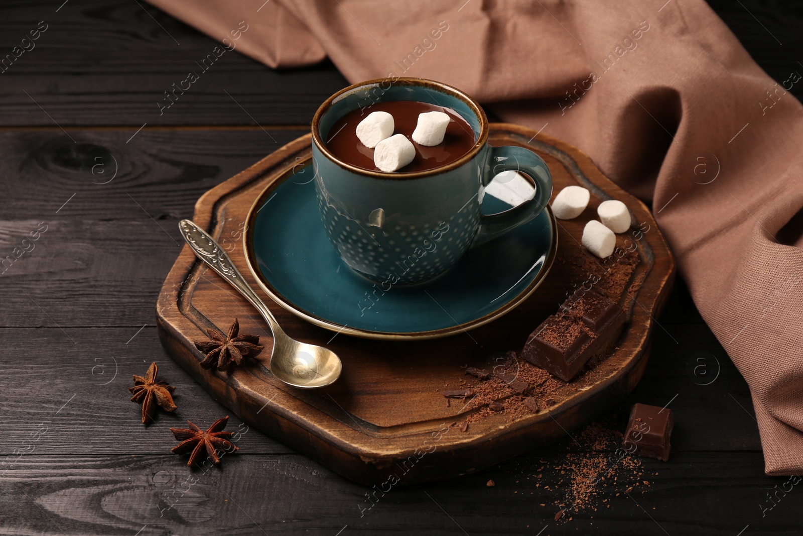 Photo of Tasty melted chocolate with marshmallows in cup and spices on dark wooden table, closeup