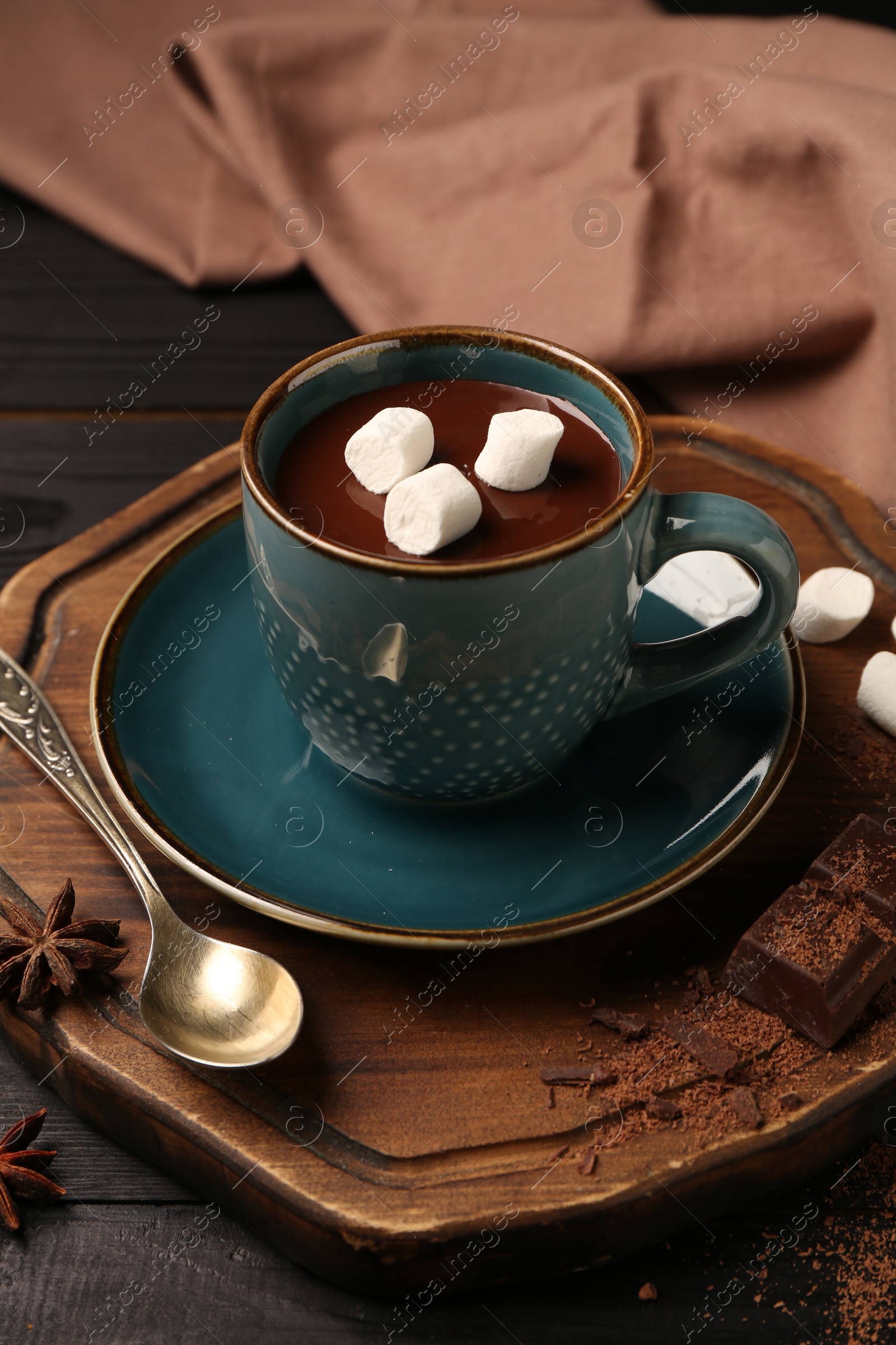 Photo of Tasty melted chocolate with marshmallows in cup and spices on wooden table, closeup