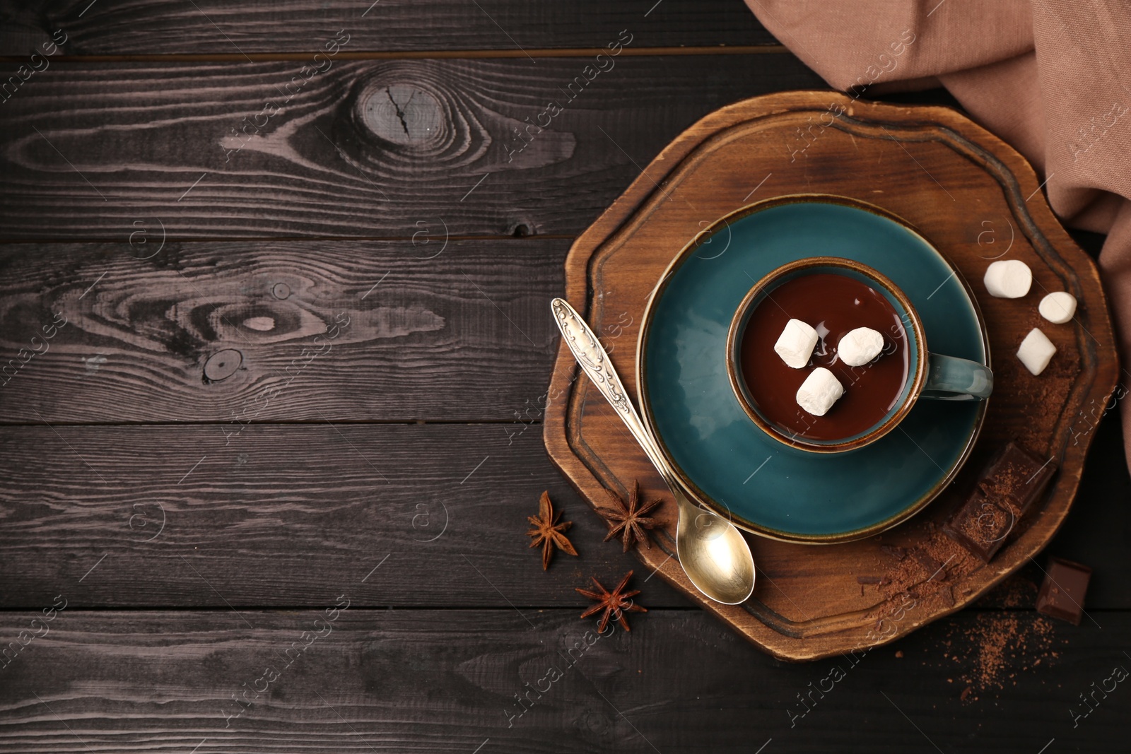 Photo of Tasty melted chocolate with marshmallows in cup and anise stars on dark wooden table, flat lay. Space for text