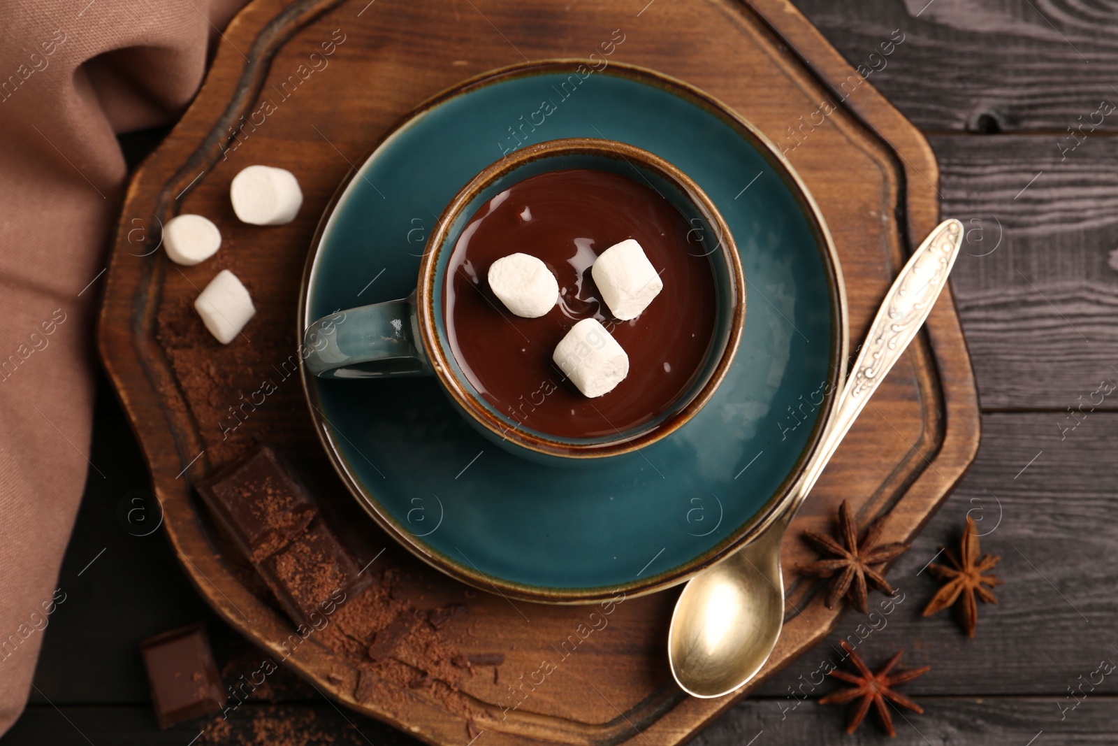 Photo of Tasty melted chocolate with marshmallows in cup and spices on dark wooden table, flat lay