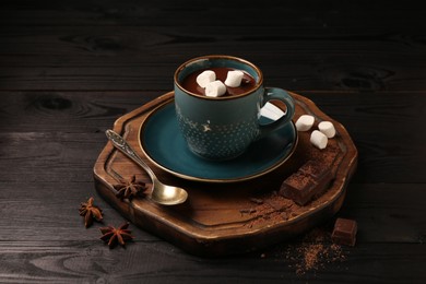 Tasty melted chocolate with marshmallows in cup and spices on dark wooden table, closeup