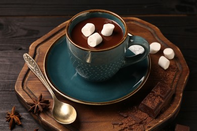 Photo of Tasty melted chocolate with marshmallows in cup and spices on dark wooden table, closeup