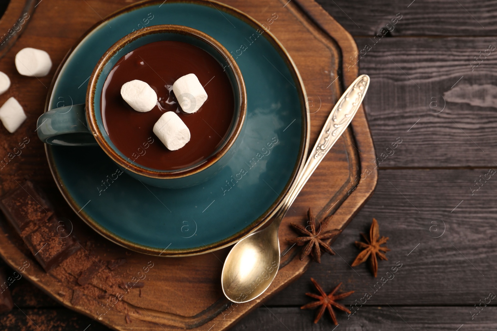 Photo of Tasty melted chocolate with marshmallows in cup and anise stars on dark wooden table, top view. Space for text