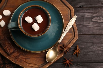 Photo of Tasty melted chocolate with marshmallows in cup and anise stars on dark wooden table, top view. Space for text