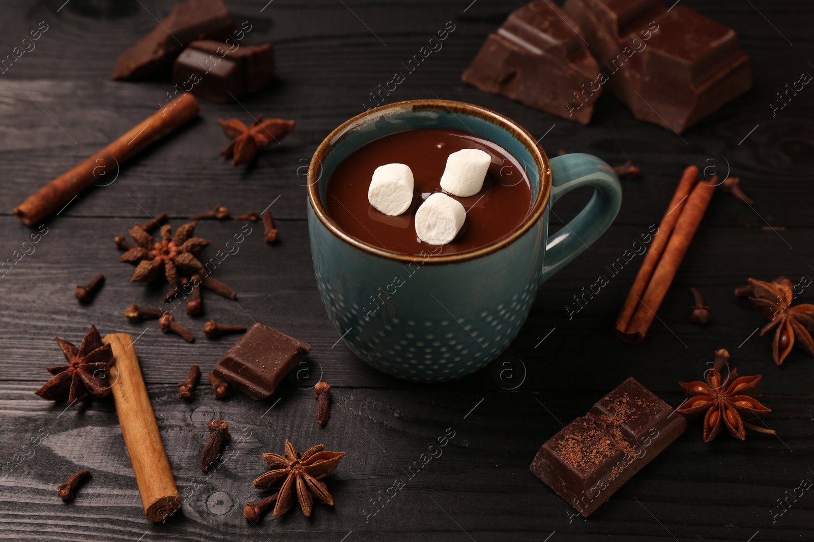 Photo of Tasty melted chocolate with marshmallows in cup and spices on dark wooden table, closeup