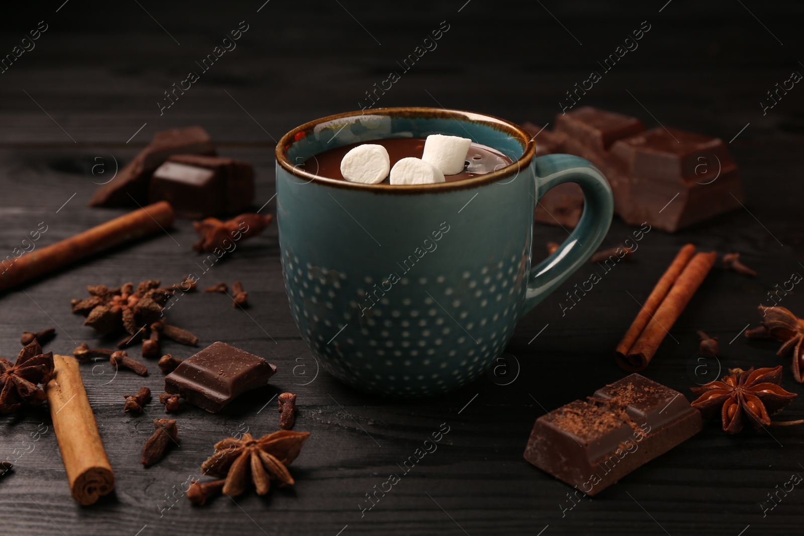 Photo of Tasty melted chocolate with marshmallows in cup and spices on dark wooden table, closeup