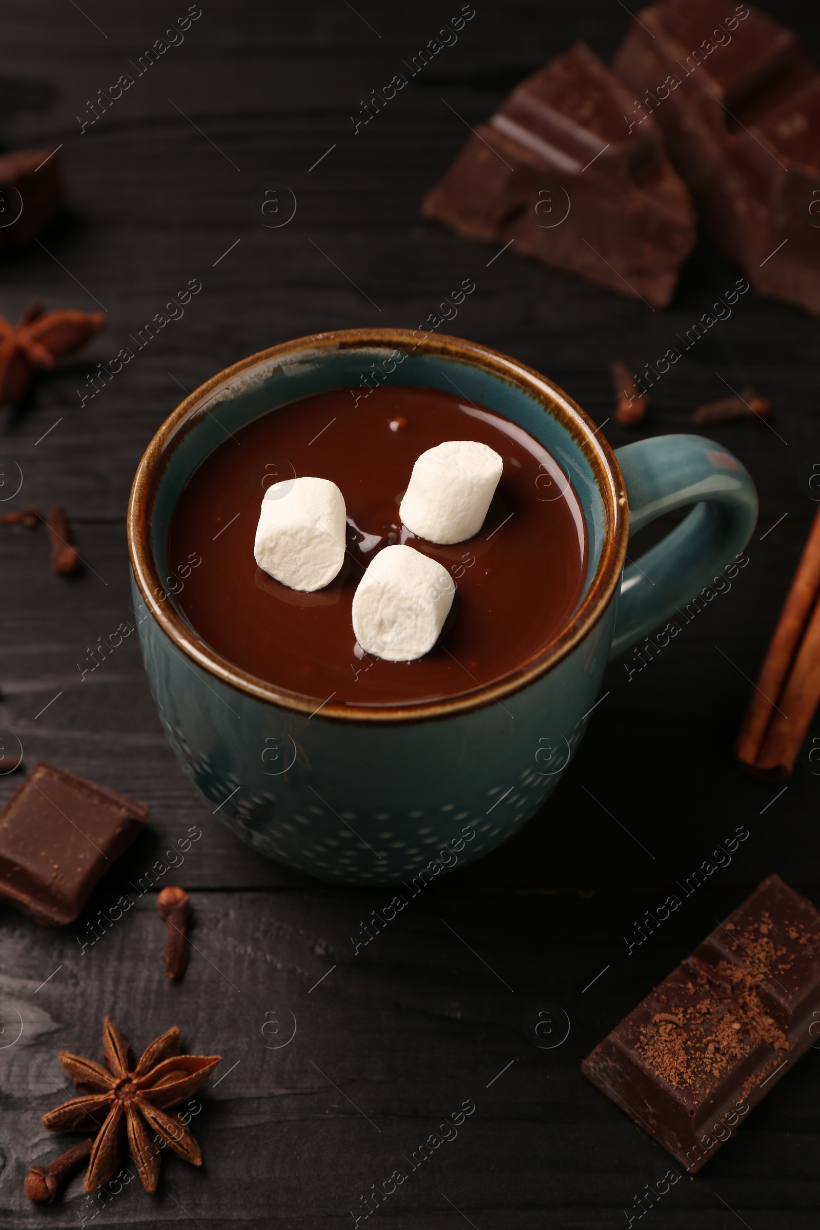 Photo of Tasty melted chocolate with marshmallows in cup and spices on dark wooden table, closeup