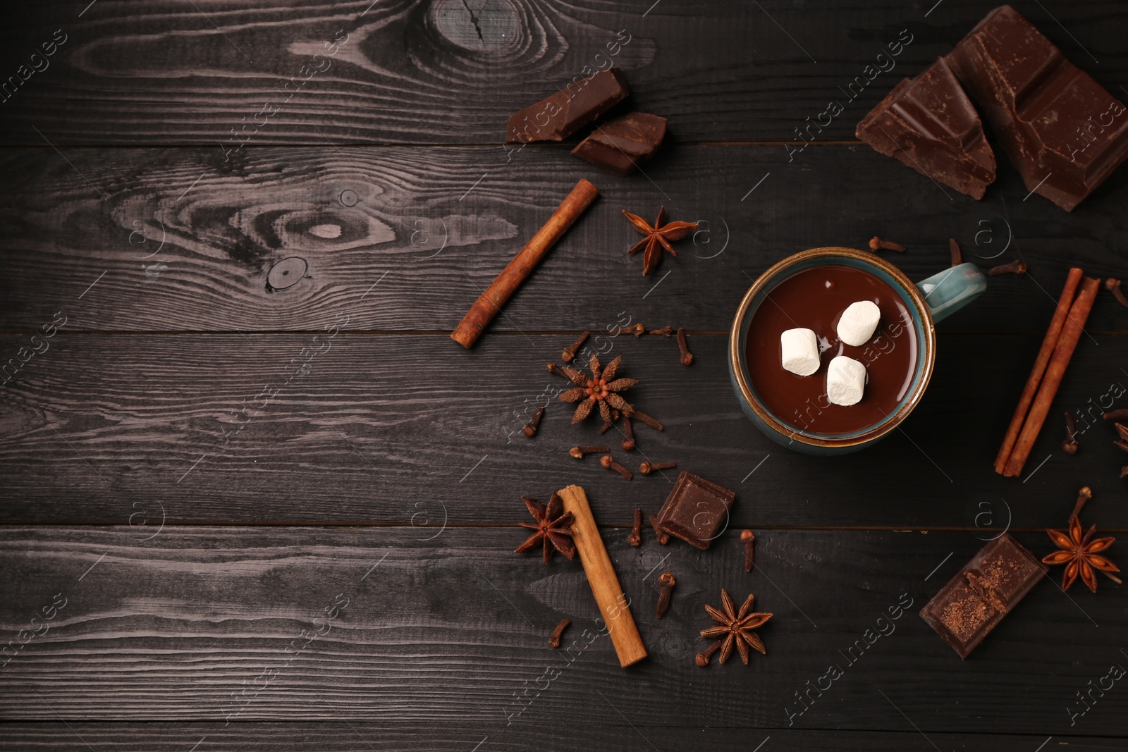 Photo of Tasty melted chocolate with marshmallows in cup and spices on dark wooden table, flat lay. Space for text