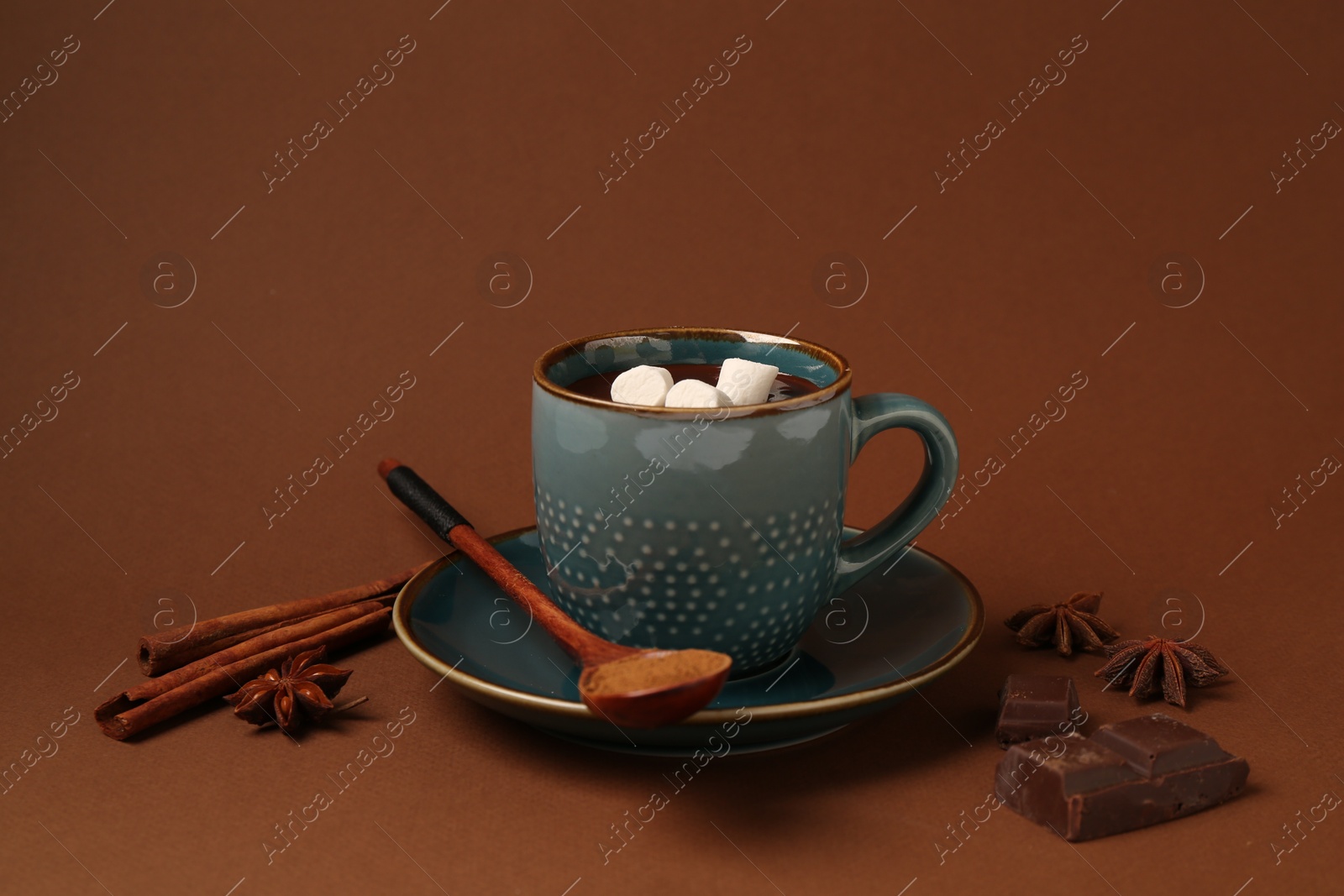 Photo of Tasty melted chocolate with marshmallows in cup and spices on brown background