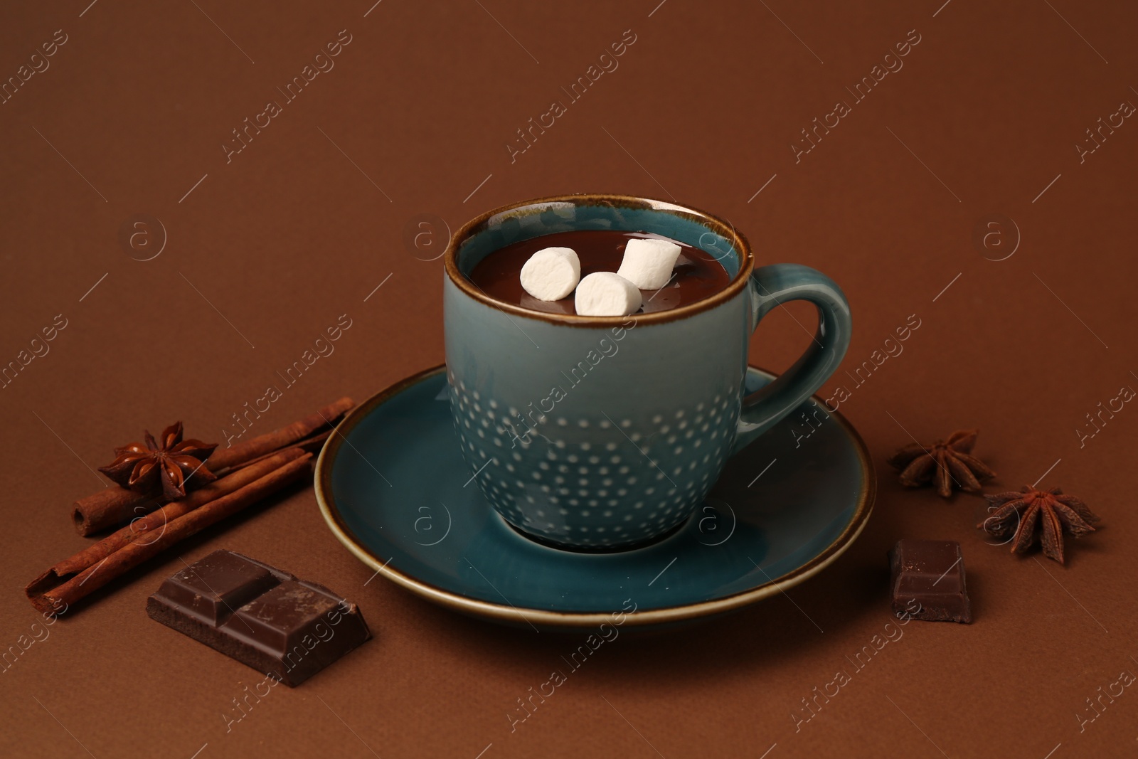 Photo of Tasty melted chocolate with marshmallows in cup and spices on brown background