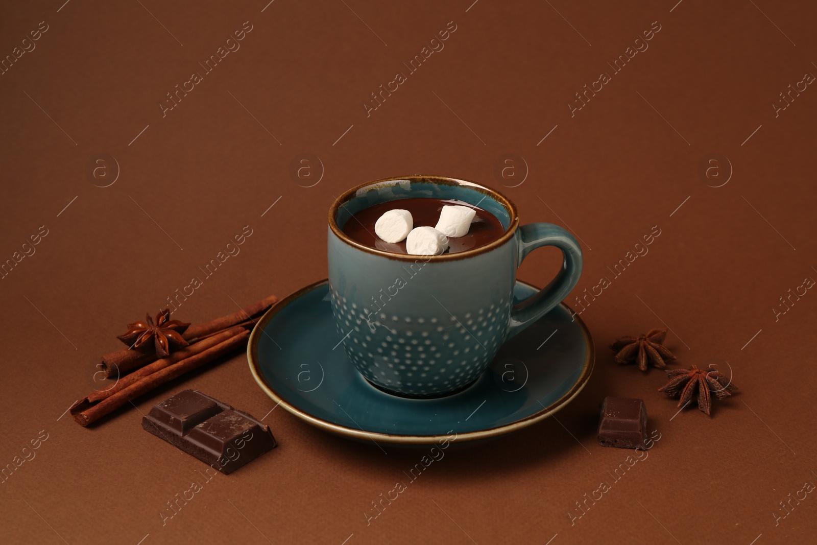 Photo of Tasty melted chocolate with marshmallows in cup and spices on brown background