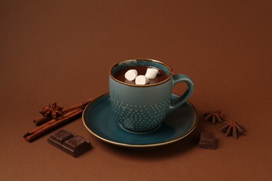 Tasty melted chocolate with marshmallows in cup and spices on brown background