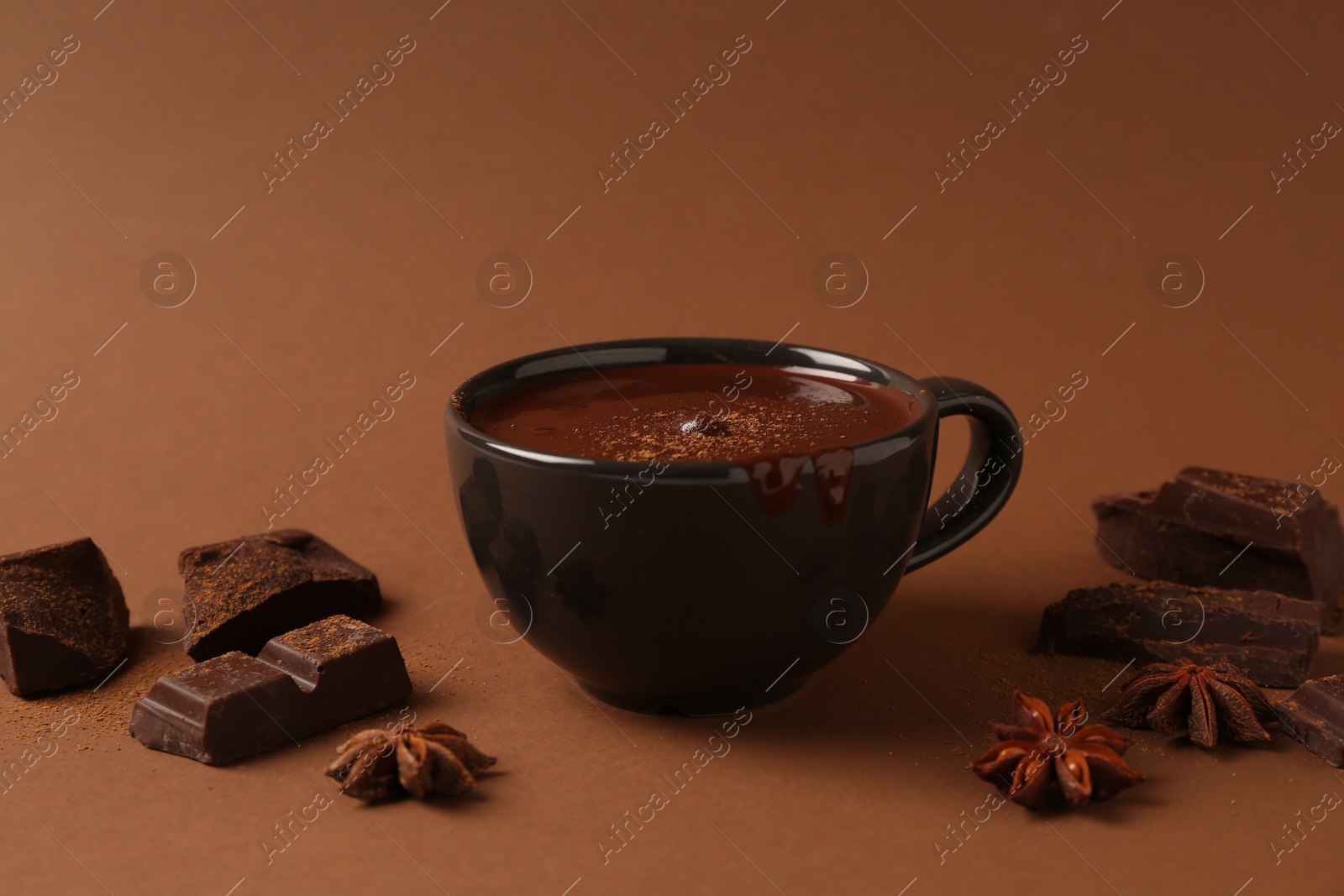 Photo of Tasty melted chocolate in cup and anise stars on brown background