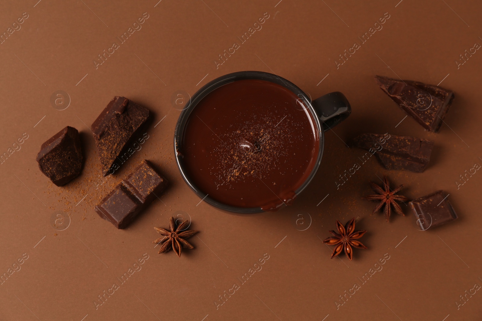 Photo of Tasty melted chocolate in cup and anise stars on brown background, flat lay