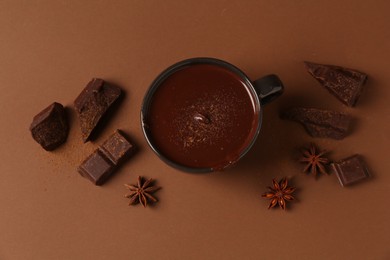 Tasty melted chocolate in cup and anise stars on brown background, flat lay