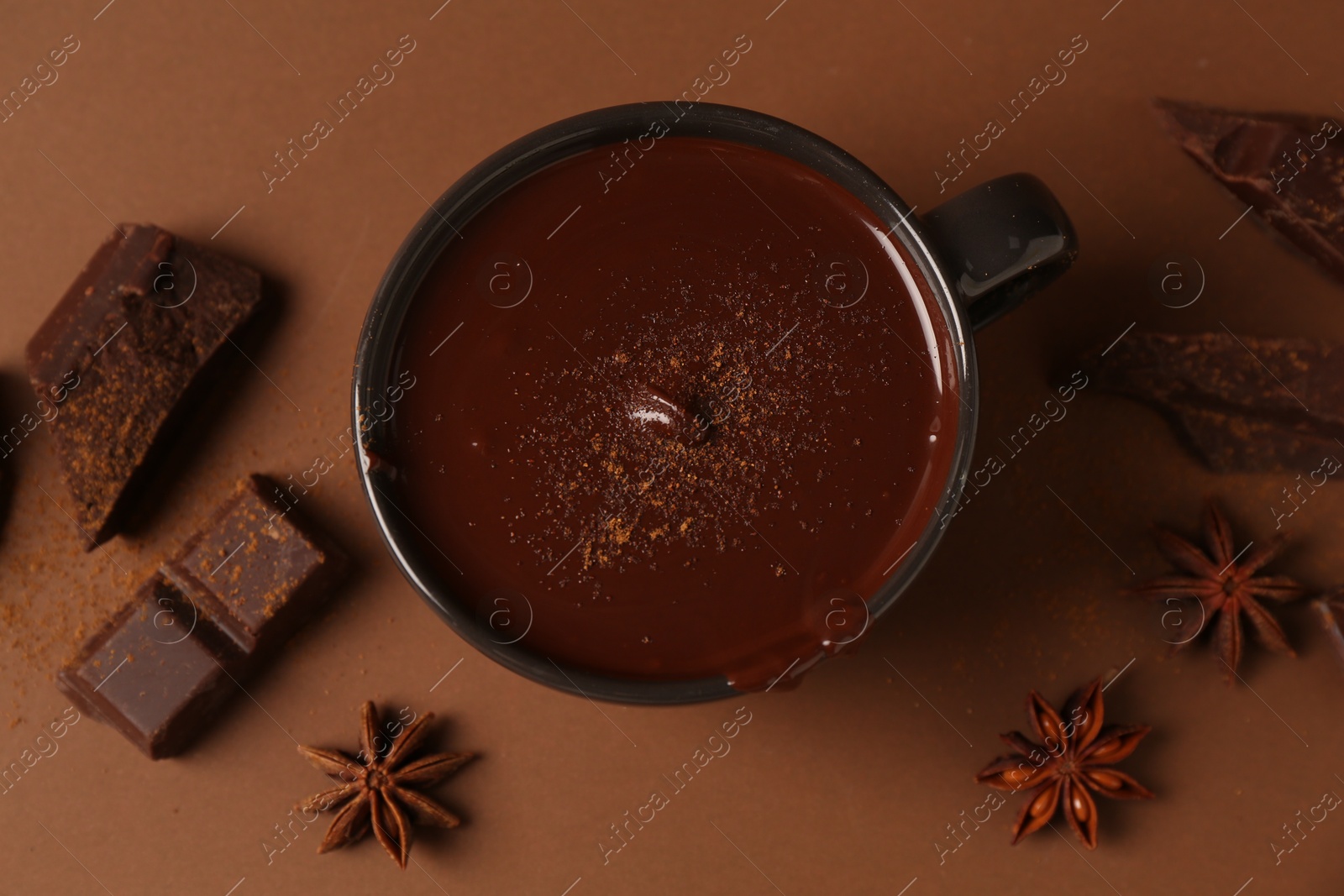 Photo of Tasty melted chocolate in cup and anise stars on brown background, flat lay