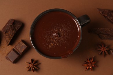 Photo of Tasty melted chocolate in cup and anise stars on brown background, flat lay