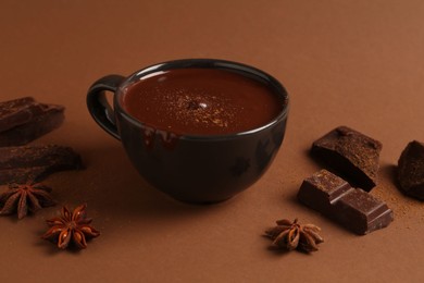 Photo of Tasty melted chocolate in cup and anise stars on brown background, closeup