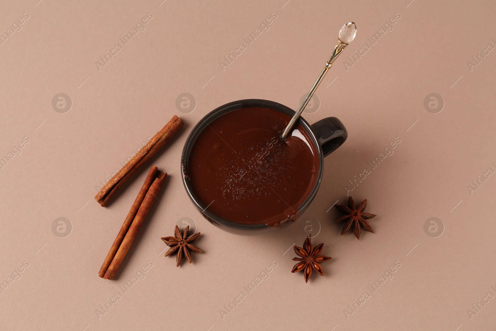 Photo of Tasty melted chocolate in cup, cinnamon sticks and anise stars on beige background, flat lay